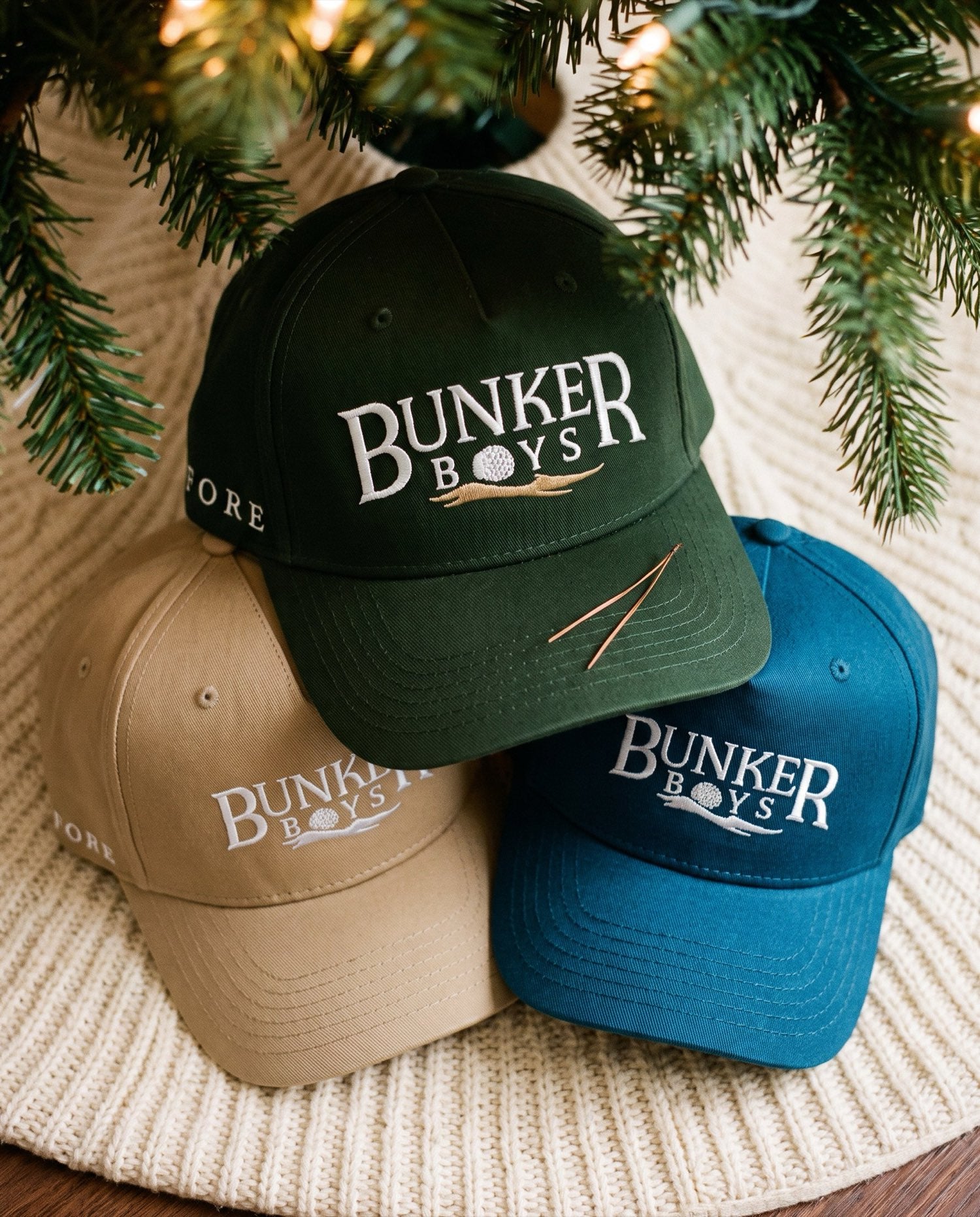 Green, beige and blue Bunker Boys hats piled under a Christmas tree.
